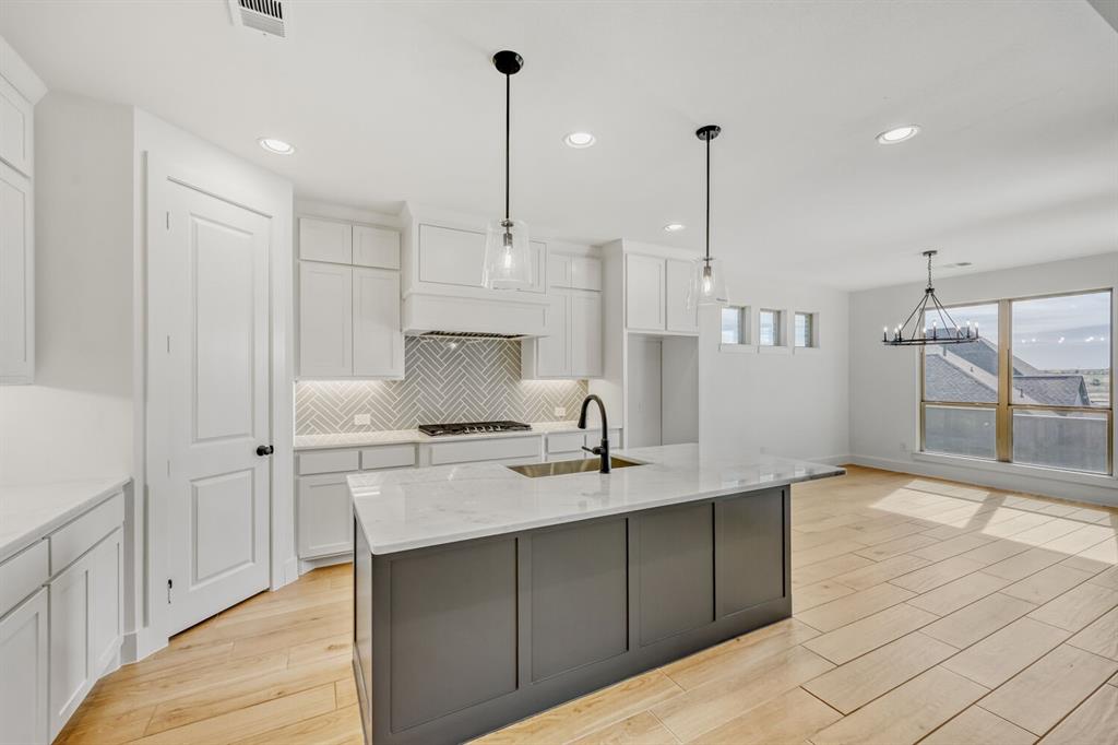 147 Derrett Lane Rhome, TX 76078 - Photo 6 of 28 Kitchen featuring light wood-type flooring, dual tone cabinetry, light stone countertops, a center island with sink, and suspended lighting