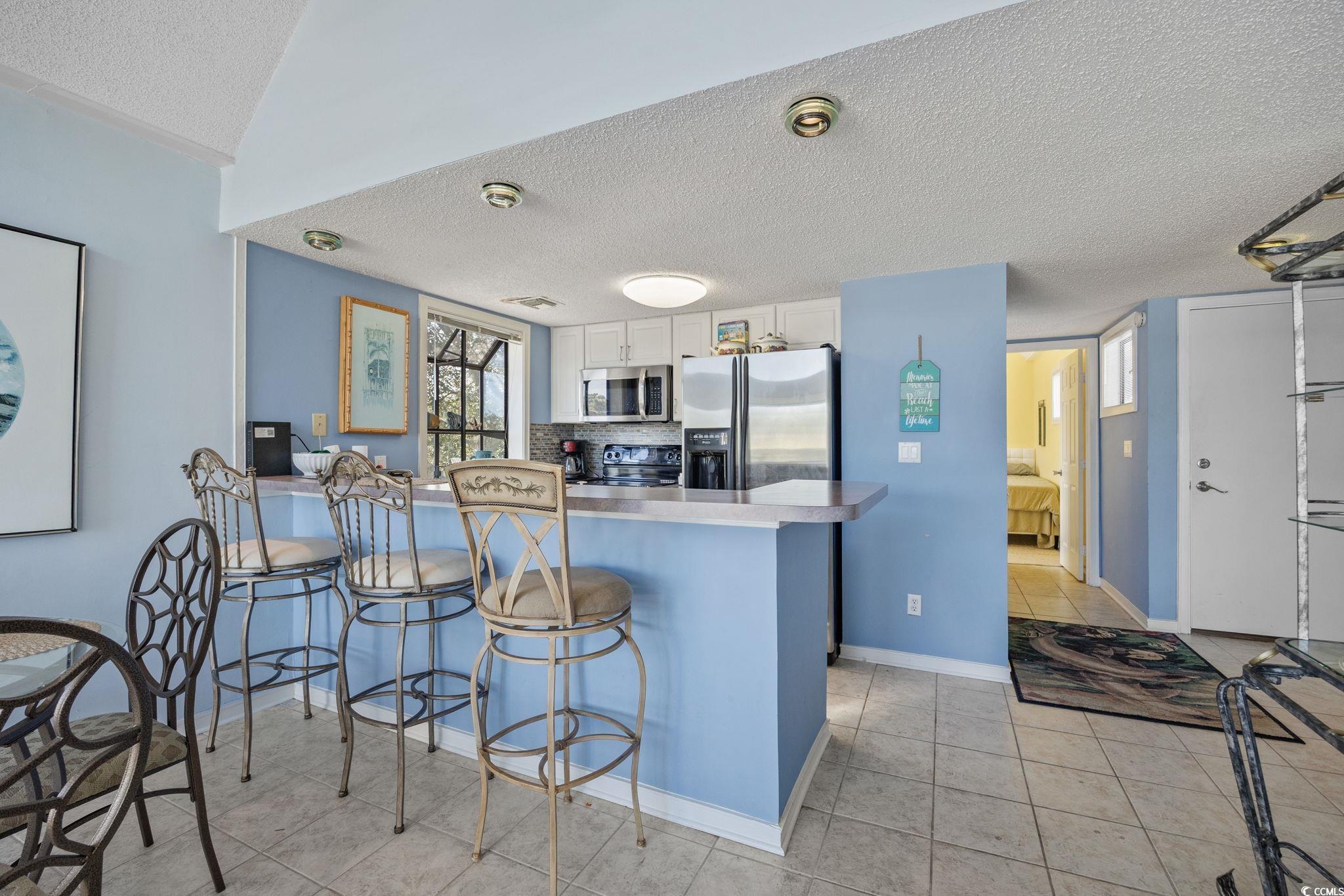 351 Lake Arrowhead Road, Unit 1301 Myrtle Beach, SC 29572 - Photo 5 of 40 Kitchen featuring a textured ceiling, a breakfast bar, a peninsula, white cabinets, and light tile patterned floors