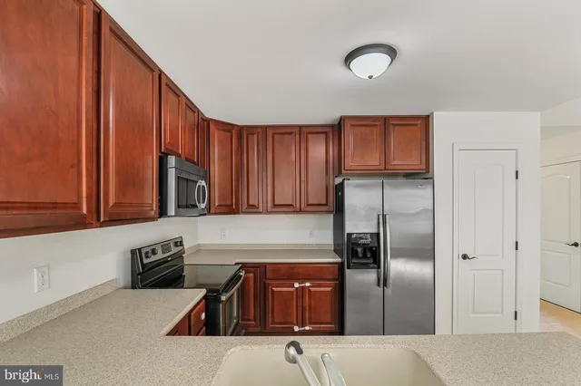 a kitchen with stainless steel appliances granite countertop a refrigerator a stove and a sink with wooden cabinets