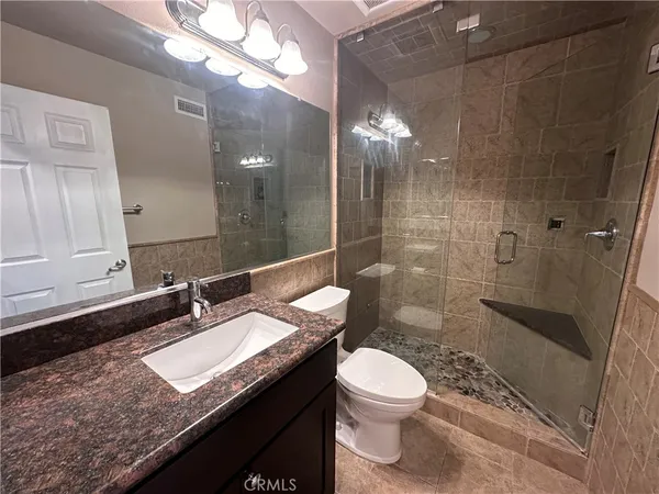 a bathroom with a granite countertop sink a toilet a mirror and shower