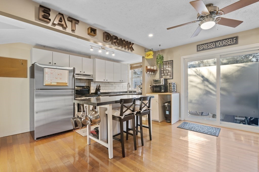 9 Sudbury Street, Unit 9 Maynard, MA 01754 - Photo 4 of 35 a kitchen with stainless steel appliances kitchen island granite countertop a table chairs in it and wooden floors