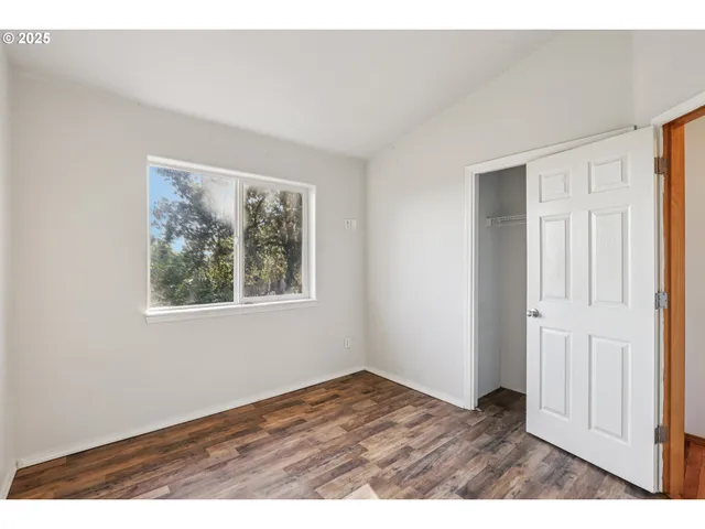 a view of an empty room with window and wooden floor