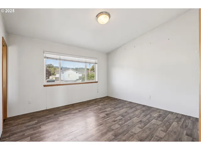 a view of an empty room with wooden floor and window