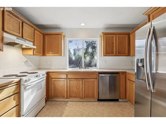 a kitchen with stainless steel appliances granite countertop a refrigerator a sink a stove and white cabinets