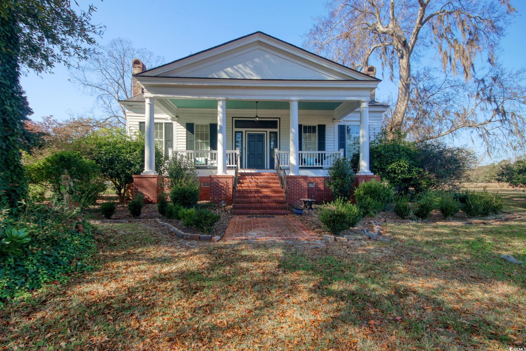 Greek revival inspired property with covered porch, a chimney, brick siding, and a front yard
