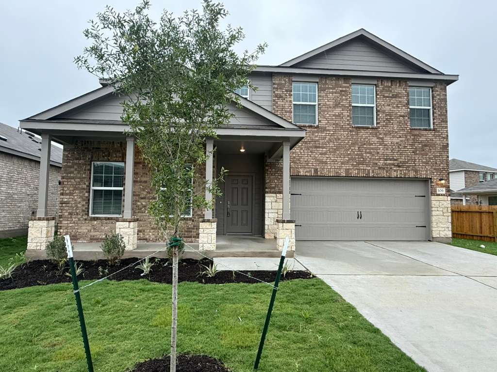 Brick and stone facade featuring a covered front porch, an attached garage, and a newly installed lawn with landscaping