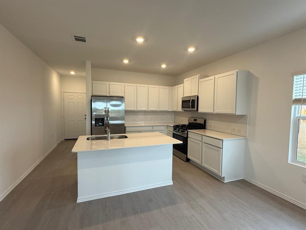 106 Brabham Loop Hutto, TX 78634 - Photo 12 of 40 Modern kitchen featuring white cabinetry, a central island with an integrated sink, stainless steel appliances, and light wood-finish flooring