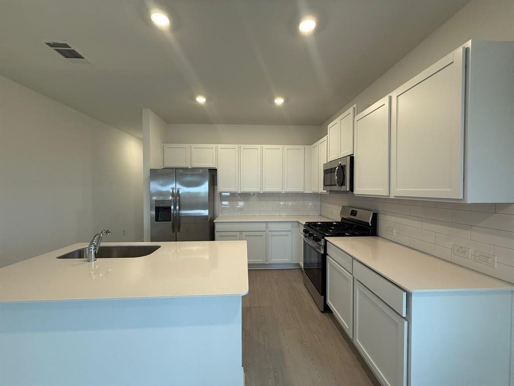 106 Brabham Loop Hutto, TX 78634 - Photo 13 of 40 Modern kitchen featuring white shaker cabinetry, stainless steel appliances, a subway tile backsplash, and light wood-finish flooring