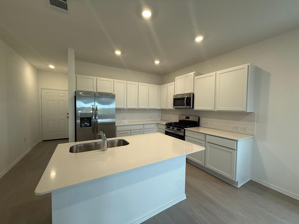 106 Brabham Loop Hutto, TX 78634 - Photo 14 of 40 Modern kitchen featuring an expansive island with an undermount sink, stainless steel appliances, white shaker cabinetry, subway tile backsplash, and recessed lighting