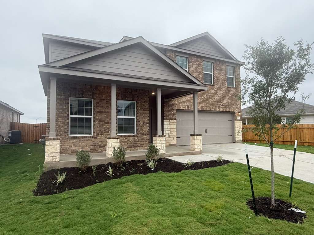 106 Brabham Loop Hutto, TX 78634 - Photo 2 of 40 Brick and stone exterior featuring a covered front porch, two-car garage, and established landscaping