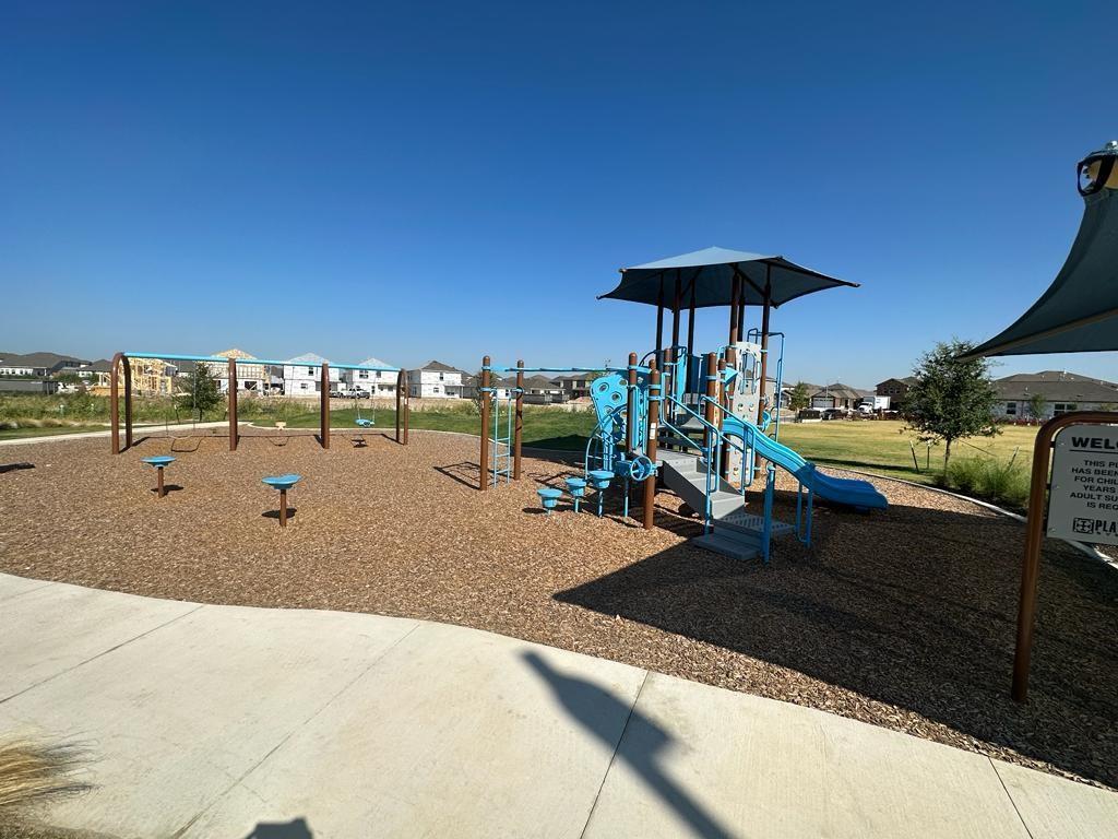 106 Brabham Loop Hutto, TX 78634 - Photo 35 of 40 Community playground featuring a blue multi-level play structure with a slide, multiple swings, and ground-level play elements, all set on a wood-chip surface