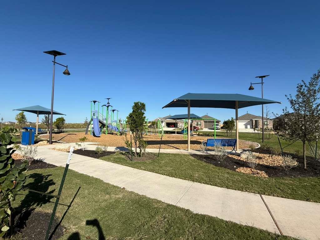 106 Brabham Loop Hutto, TX 78634 - Photo 39 of 40 Community park featuring a playground, shade structures, paved walking paths, benches, and landscaped areas with young trees and shrubs