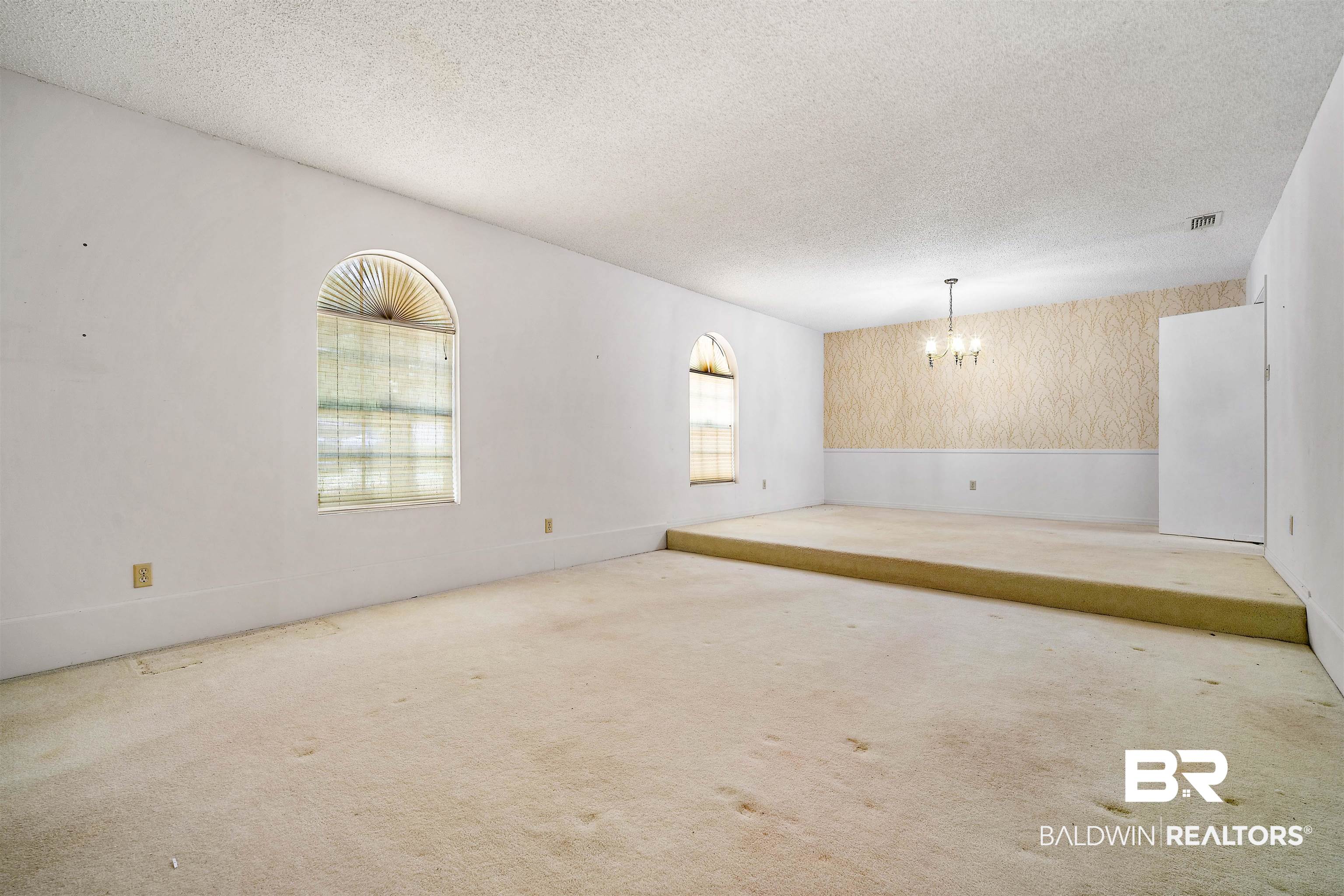 5559 Woodside Drive North Mobile, AL 36608 - Photo 20 of 28 Unfurnished living room featuring a textured ceiling, a chandelier, carpet flooring, wainscoting, and wallpapered walls