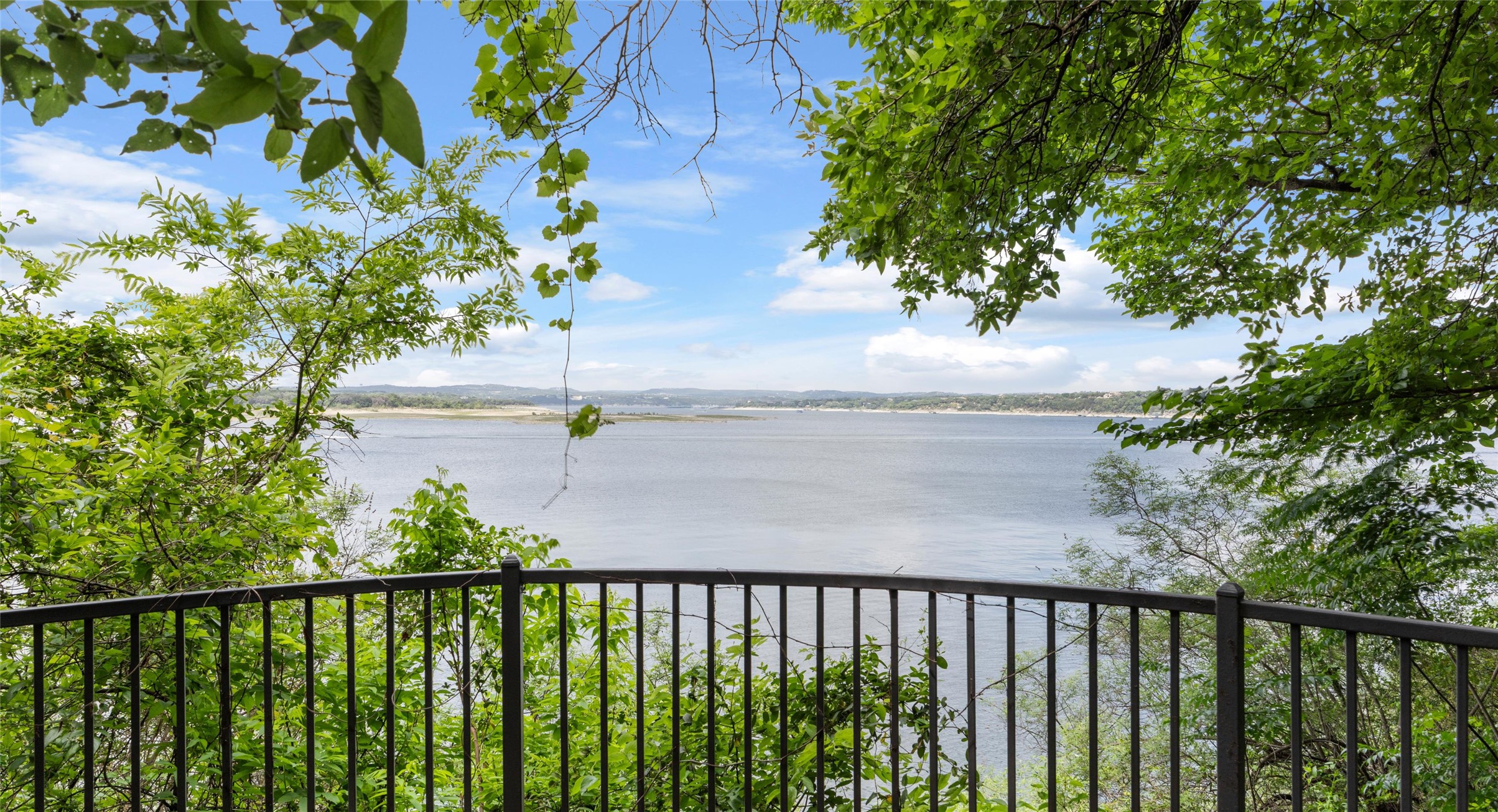 2918 Ranch Road 620 North, Unit C122 Austin, TX 78734 - Photo 30 of 36 The property features a balcony with a black metal railing, offering expansive views of the water and distant shoreline under a blue sky with clouds