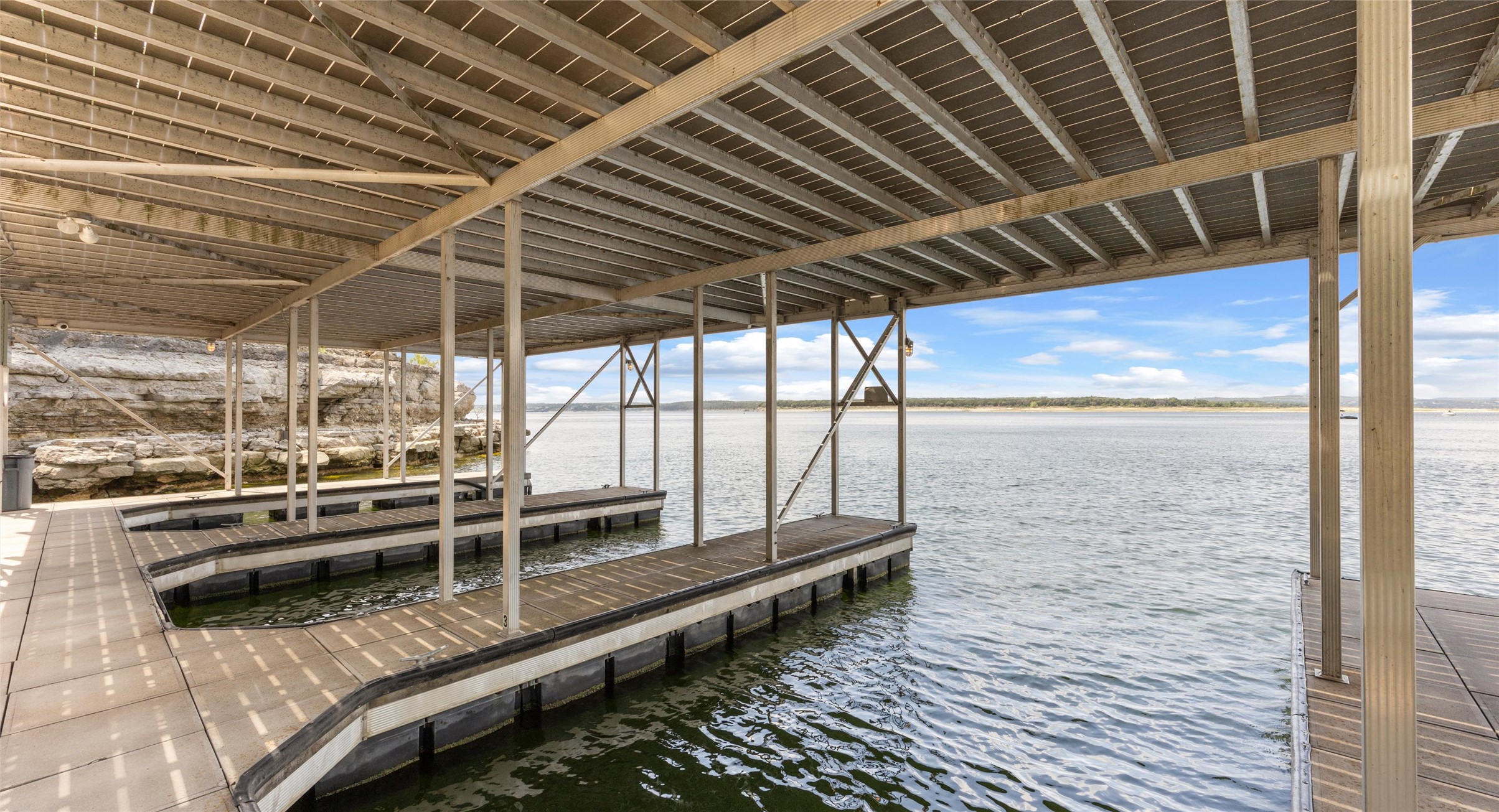 2918 Ranch Road 620 North, Unit C122 Austin, TX 78734 - Photo 31 of 36 Covered boat docks with direct access to the water, featuring a metal roof structure and a rocky shoreline in the background