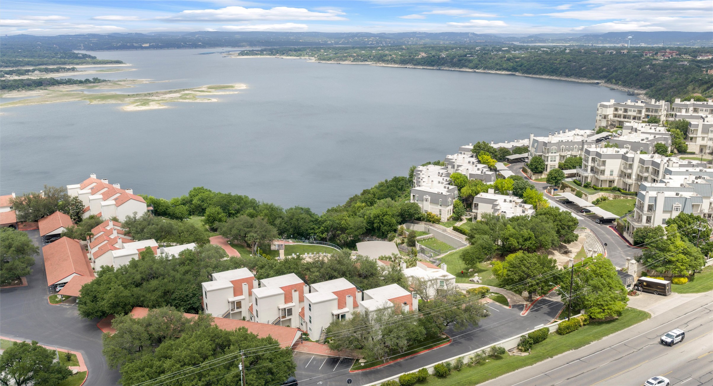 2918 Ranch Road 620 North, Unit C122 Austin, TX 78734 - Photo 34 of 36 The property features a serene lake view with surrounding green hills, and is situated within a community of residences with diverse architectural styles, including buildings with white facades and red-tiled roofs, and others with light-colored exteriors and grey roofs