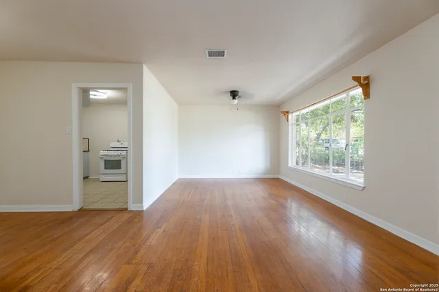a view of an empty room with wooden floor and a window