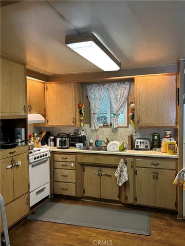 a kitchen with stainless steel appliances a white refrigerator a sink a stove and white cabinets with wooden floor