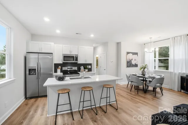 a kitchen with stainless steel appliances granite countertop a stove a refrigerator a sink a dining table and chairs with wooden floor