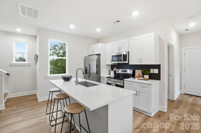 a kitchen with stainless steel appliances granite countertop a stove a refrigerator a sink dishwasher a dining table and chairs with wooden floor