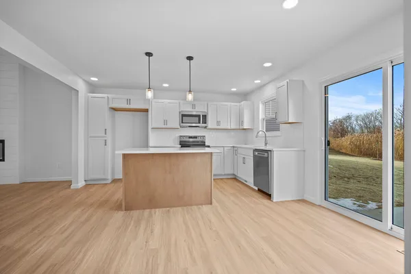 a large kitchen with kitchen island a island a stove a refrigerator a sink dishwasher and white cabinets with wooden floor