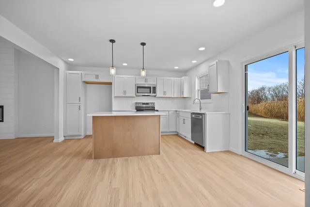 a large kitchen with kitchen island a island a stove a refrigerator a sink dishwasher and white cabinets with wooden floor