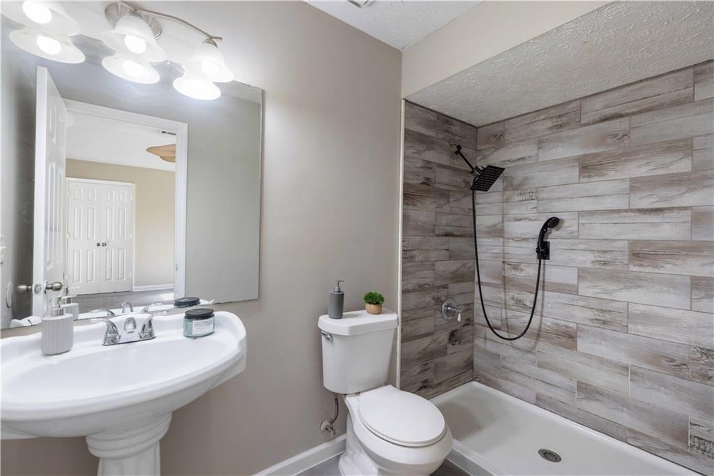 4 Ford Road Phenix City, AL 36869 - Photo 17 of 52 Pedestal sink, wall-mounted mirror, wood-look tiled shower surround, matte black shower fixtures, and a ceiling-mounted light fixture