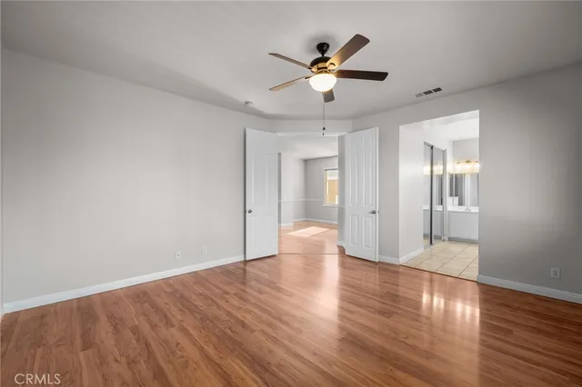 a view of an empty room with wooden floor and a ceiling fan