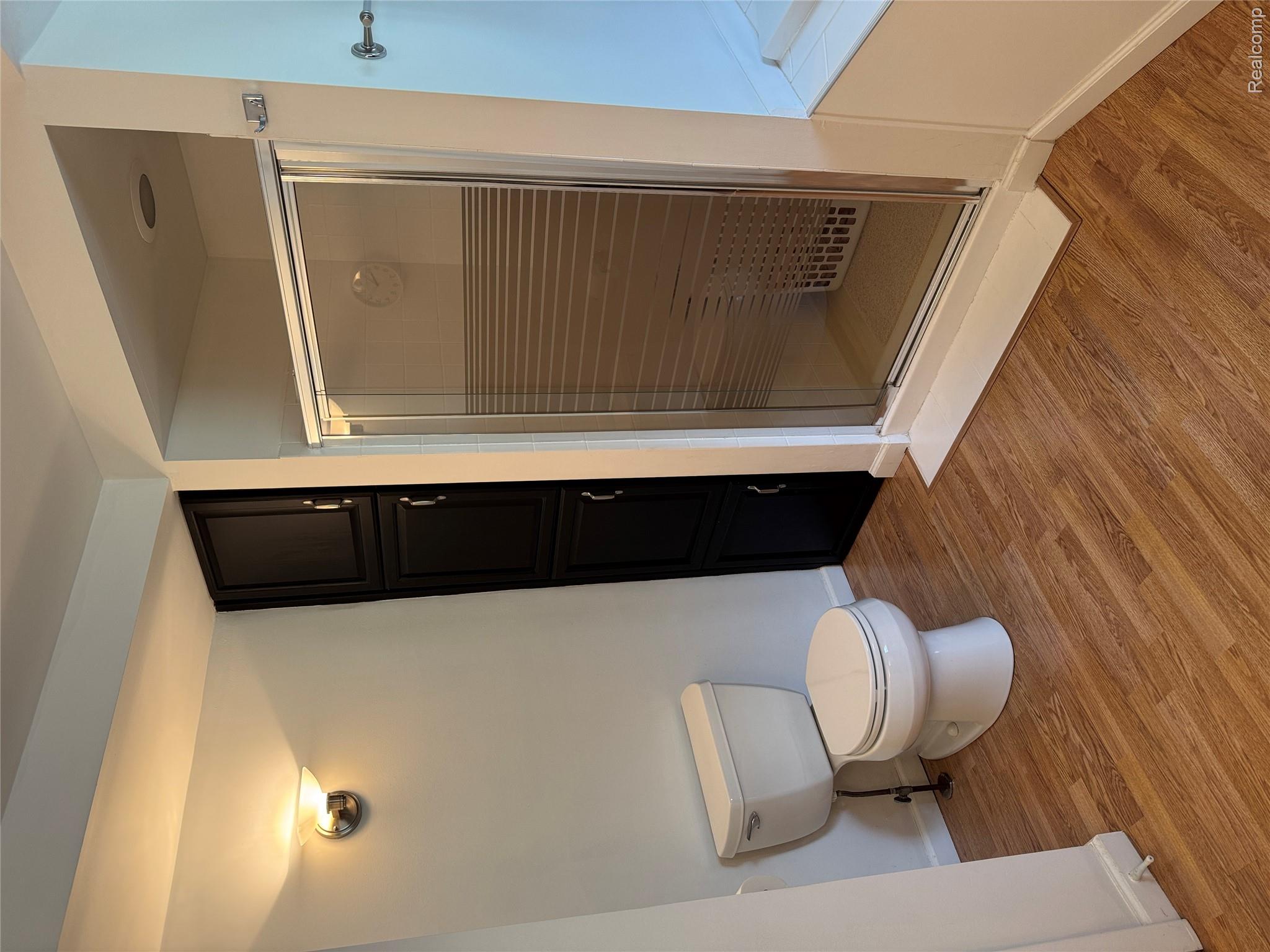 3138 Ponemah Drive Fenton, MI 48430 - Photo 7 of 19 Bathroom featuring a glass-enclosed shower, wood-finish flooring, a white toilet, and dark built-in cabinetry