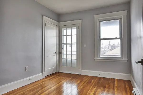 a view of an empty room with wooden floor and a window