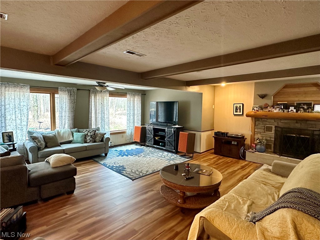 48224 Walnut Valley Road Wellington, OH 44090 - Photo 12 of 48 Living room with a fireplace, a textured ceiling, beamed ceiling, light hardwood / wood-style flooring, and ceiling fan