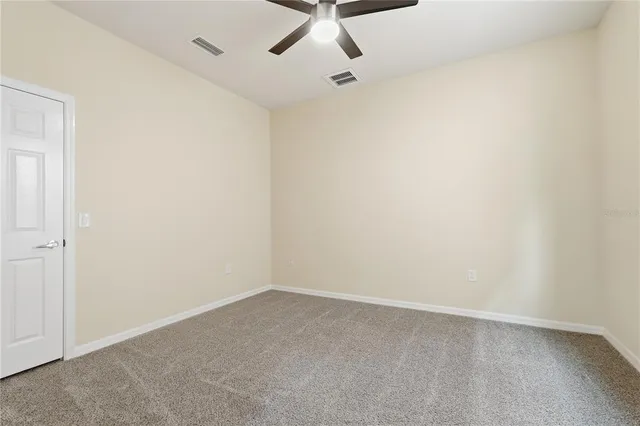 an empty room with a ceiling fan and carpet