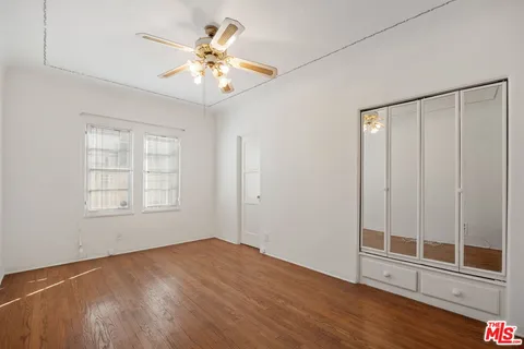 an empty room with wooden floor fan and windows