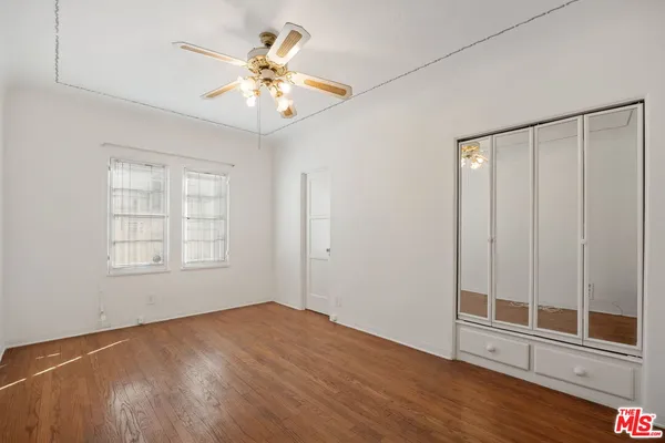 an empty room with wooden floor fan and windows