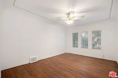 an empty room with wooden floor fan and windows