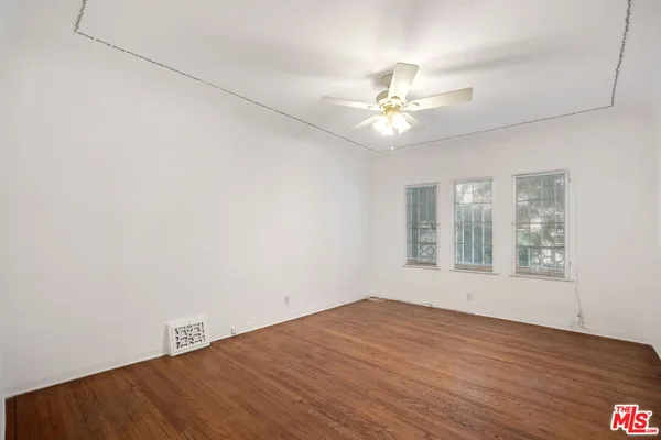 an empty room with wooden floor fan and windows