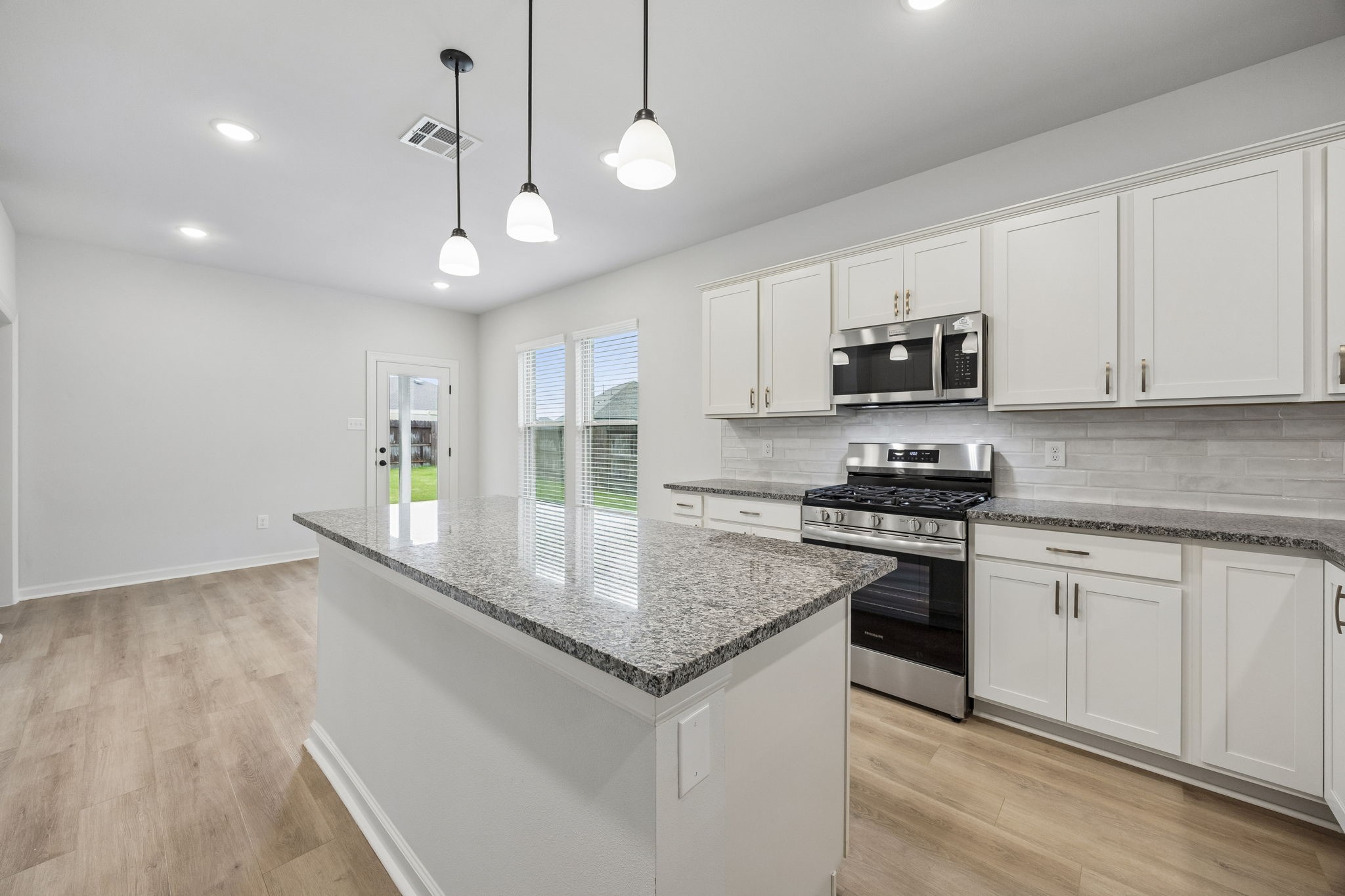 10902 Bonfire Trail Beasley, TX 77417 - Photo 7 of 36 This modern kitchen features sleek granite countertops, white cabinetry, and stainless steel appliances. It boasts ample natural light and a spacious layout, complete with a central island and stylish pendant lighting.