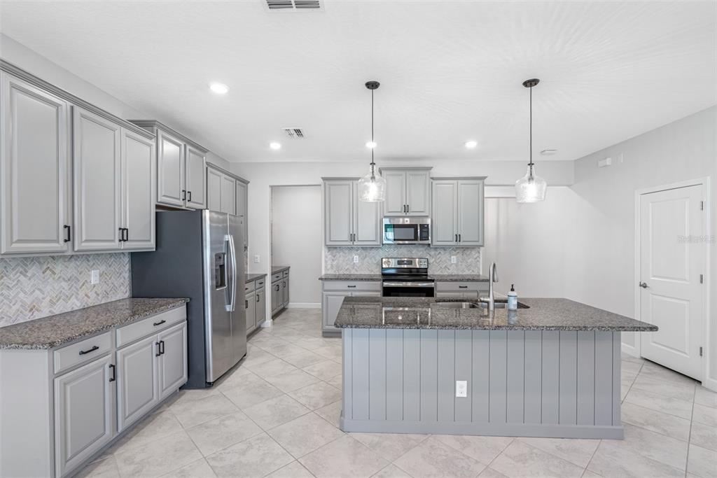 13333 Orca Sound Drive Riverview, FL 33579 - Photo 8 of 32 a kitchen with kitchen island granite countertop a stove a sink a refrigerator and white cabinets with wooden floor