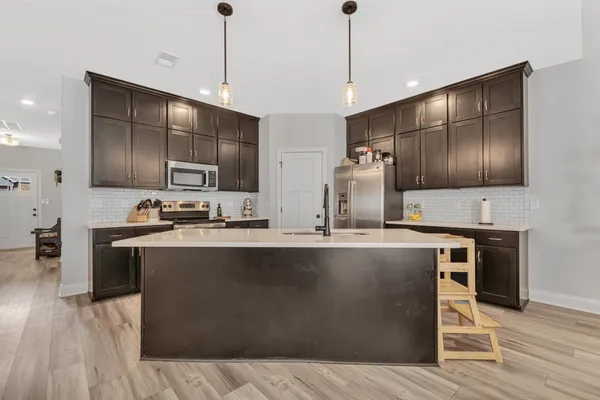 a kitchen with stainless steel appliances granite countertop a sink a stove and kitchen island with wooden floor