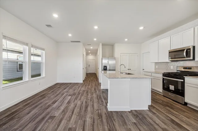 a large kitchen with stainless steel appliances a large counter top a stove a sink dishwasher a refrigerator and a microwave oven with wooden floor