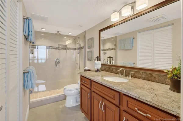 a bathroom with a granite countertop sink a toilet a mirror and shower