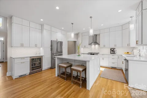 a large white kitchen with a stove a sink a kitchen island with chairs and wooden floor