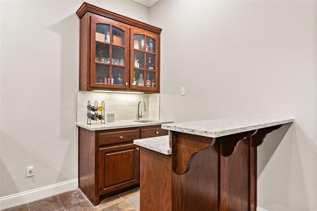 517 Chado Lane Robinson, TX 76706 - Photo 8 of 40 Indoor wet bar featuring a textured wall, decorative backsplash, glass fronted cabinets, light stone counters, and stone finish floors