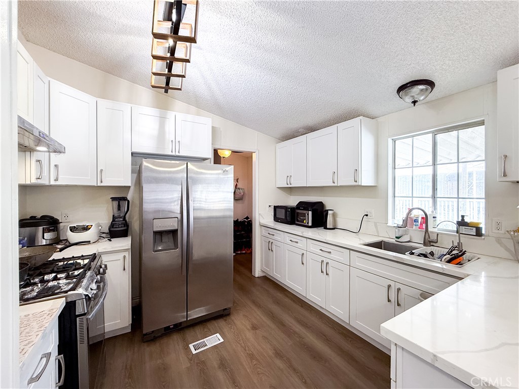 1855 East Riverside, Unit 130 Ontario, CA 91761 - Photo 25 of 62 a kitchen with a refrigerator a sink dishwasher a stove and white cabinets with wooden floor
