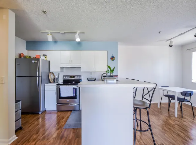 a kitchen with stainless steel appliances a refrigerator a stove a sink dishwasher and a dining table with wooden floor