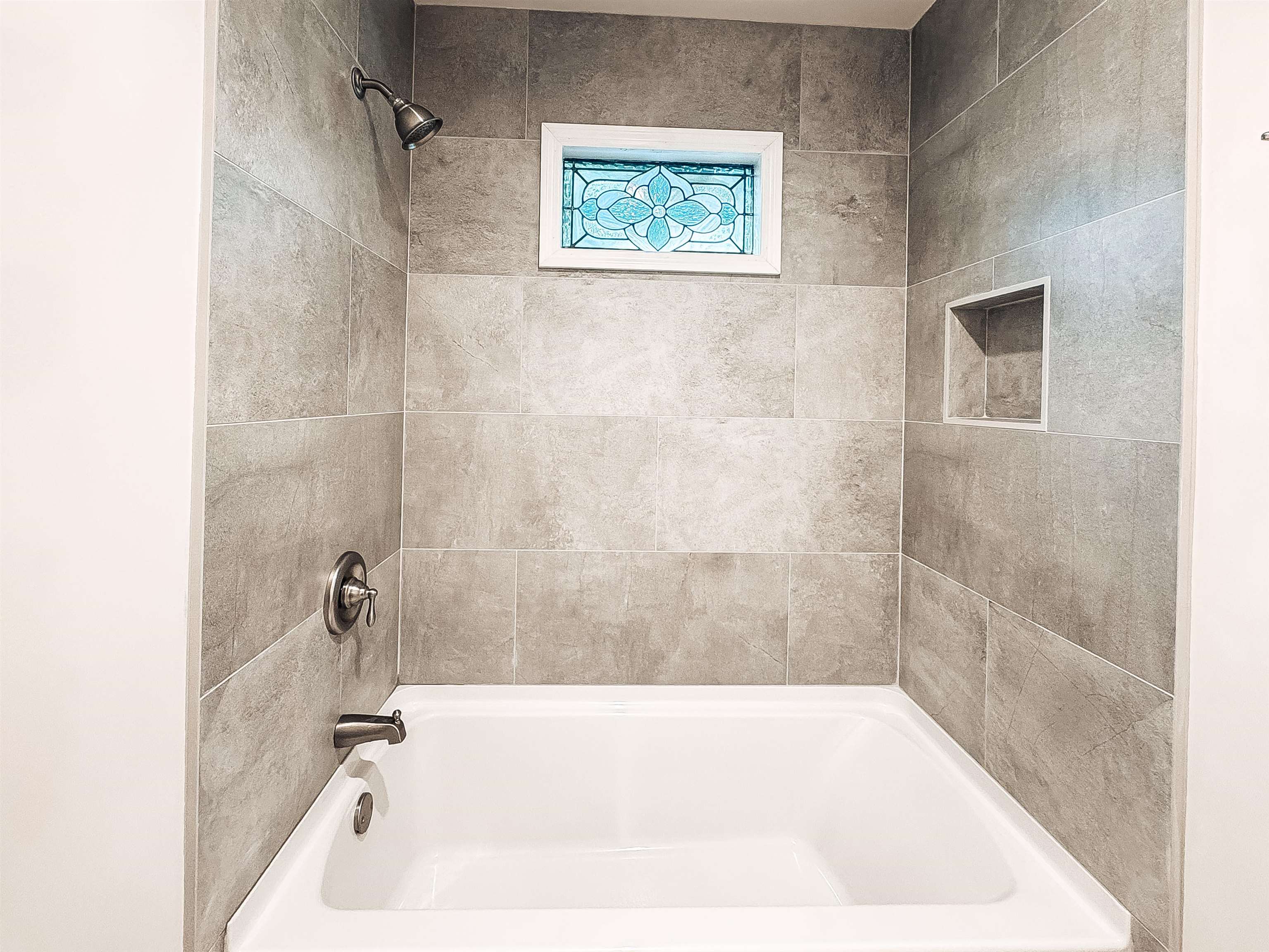 832 South Tree Drive Collierville, TN 38017 - Photo 33 of 40 Bathtub with surrounding large format gray tile, oil-rubbed bronze shower fixtures, a decorative stained-glass window, and a recessed shower niche