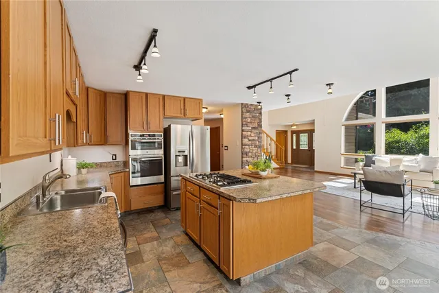 a kitchen with stainless steel appliances granite countertop a stove top oven a sink dishwasher a dining table and chairs with wooden floor