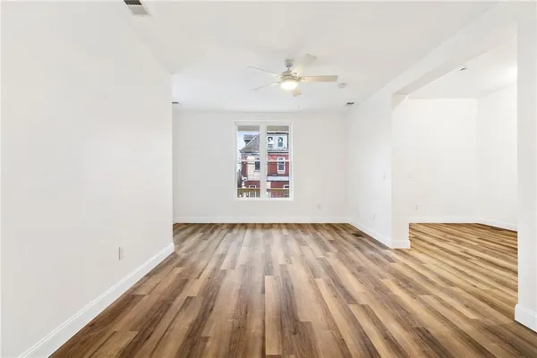 an empty room with wooden floor chandelier fan and windows