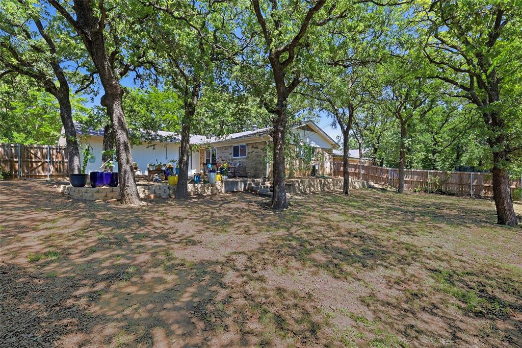 16 Coffee Tavern Road Bedford, TX 76022 - Photo 21 of 24 Expansive rear yard featuring mature trees, a wood privacy fence, and a stone retaining wall