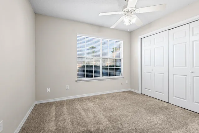 an empty room with chandelier fan and windows